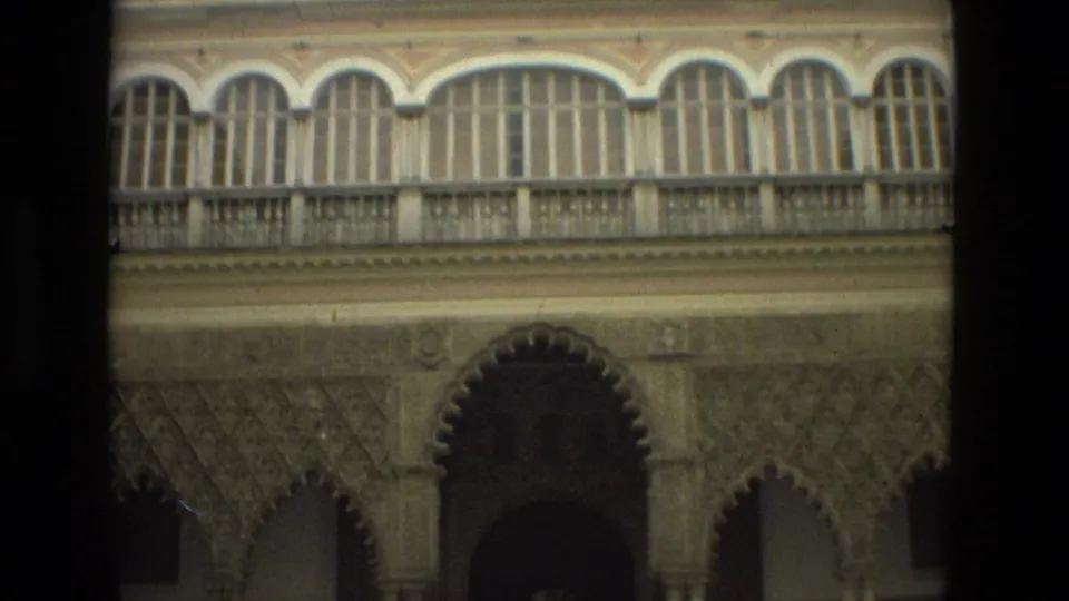 1978 8mm view of a Seville courtyard facade with upper arched windows, carved walls, and a shadowed entrance.