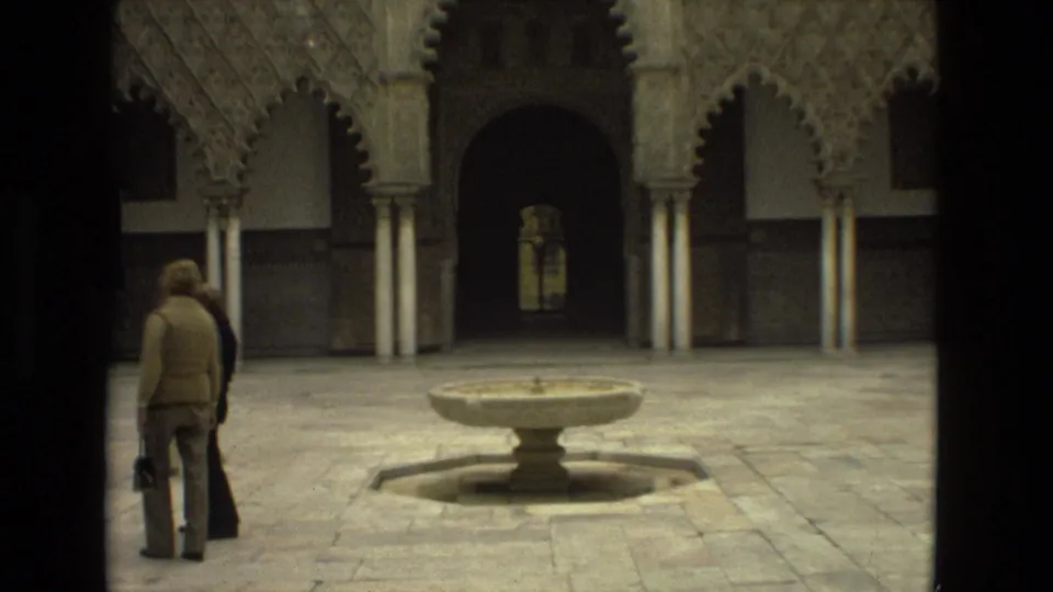 1978 8mm Seville footage showing visitors near a stone fountain, with carved arches and a dark doorway behind them.