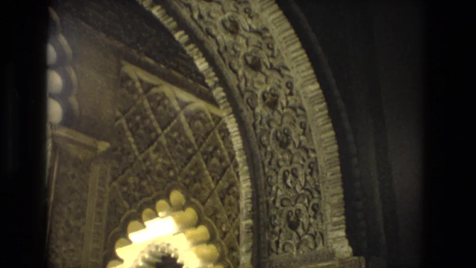 Close 8mm view of ornate arch carving in Seville, with patterned surfaces, deep shadow, and a bright scalloped opening.