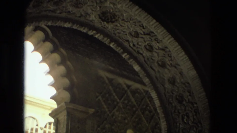 8mm frame from Seville showing carved archwork, a bright exterior opening, and pale architectural detail beyond the shadowed foreground.