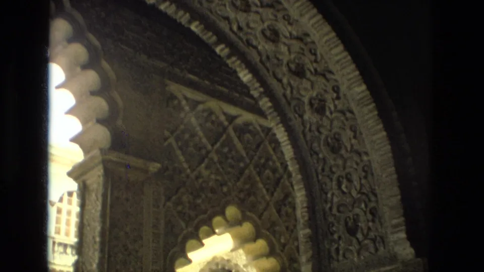 1978 8mm frame from Seville showing a Moorish-style horseshoe arch, carved decorative surfaces, and sunlit architectural detail.