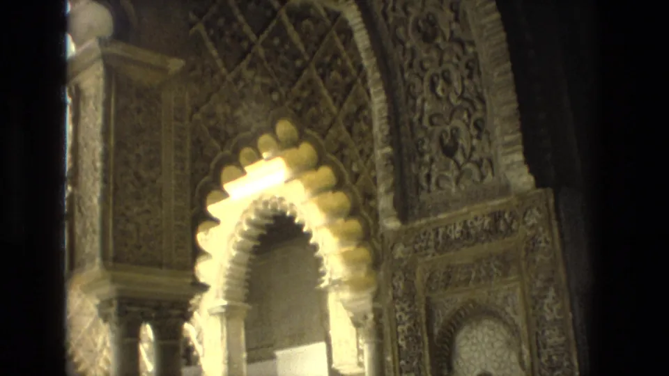 1978 Seville home-movie frame showing a bright horseshoe arch, slender columns, carved ornament, and geometric tilework along the lower wall.