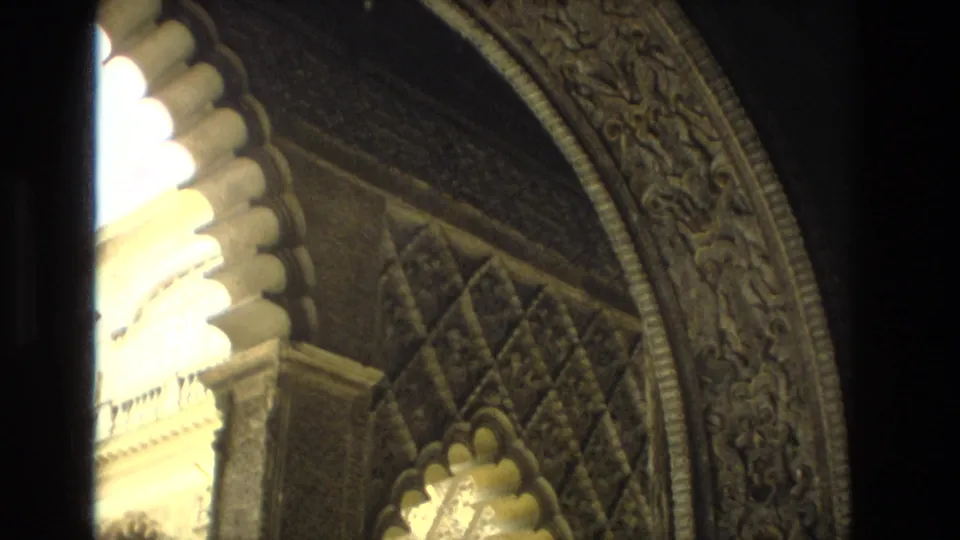 1978 Seville frame showing bright light through an arch beside carved Moorish-style wall ornament and dark doorway framing.