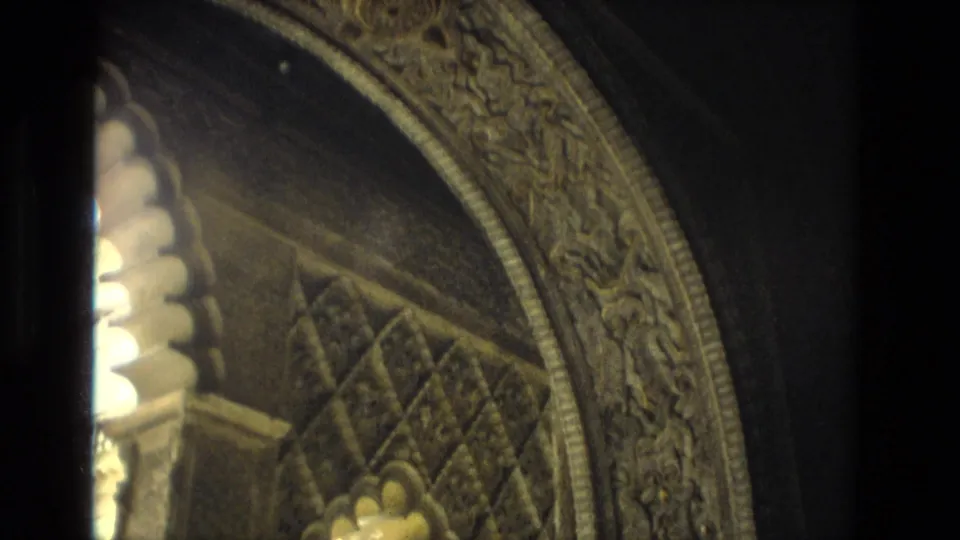 1978 Seville frame with a Moorish-style arch, carved decorative band, patterned surfaces, and a dark vertical obstruction from the camera position.