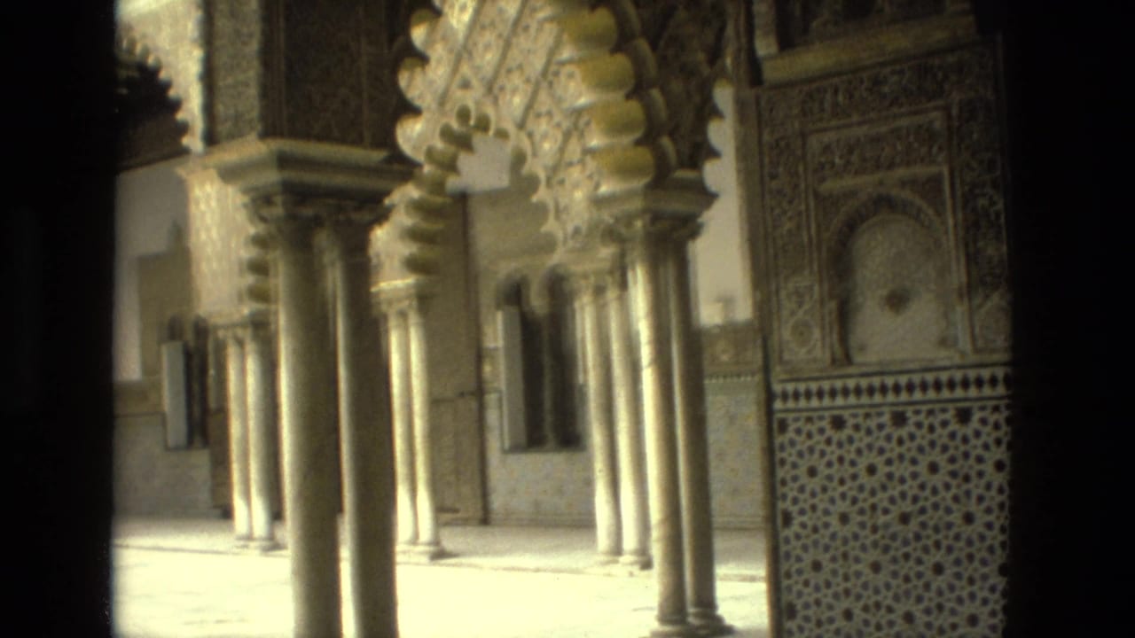 Sunlit arches and slender columns with patterned wall tilework in a historic interior courtyard.