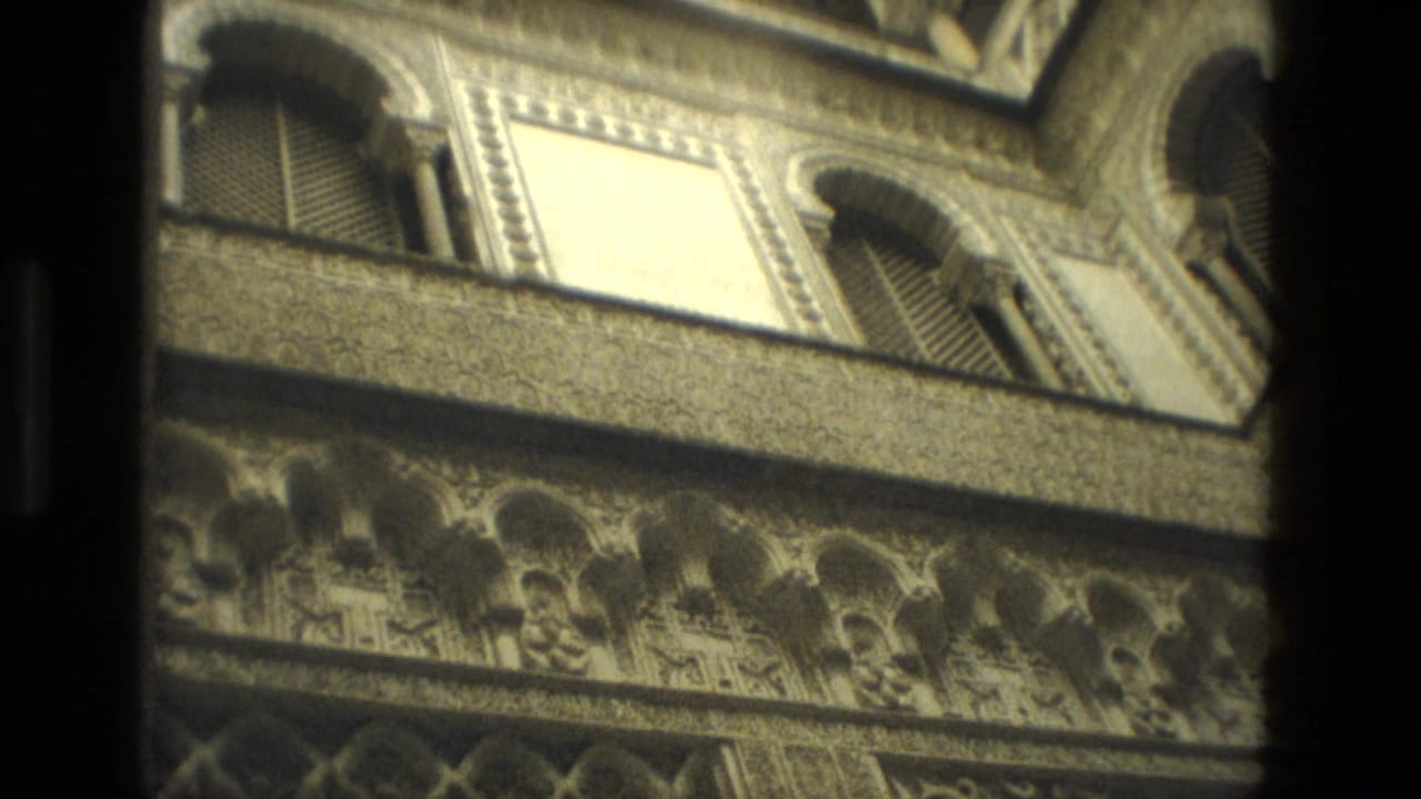 1978 Seville 8mm view of ornate arched stonework and shuttered upper windows, partially obscured by dark interior framing.