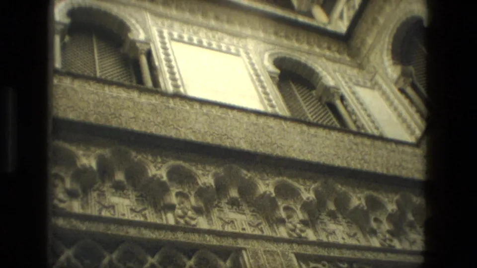 1978 Seville 8mm view of ornate arched stonework and shuttered upper windows, partially obscured by dark interior framing.
