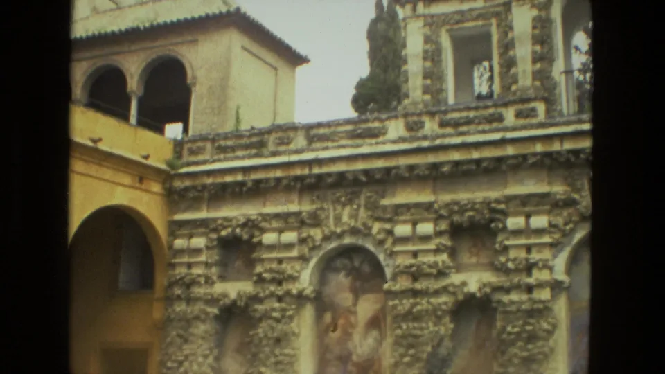 Seville 1978 home-movie frame of a historic courtyard with yellow arches, pool reflection, carved wall detail, and upper galleries.