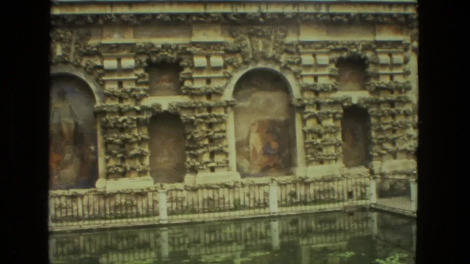 1978 Seville 8mm frame showing an ornate facade, painted niches, balustrade, and a reflective pool in the foreground.