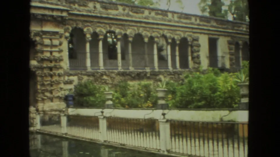 1978 Seville garden view with arched stone windows, dense plantings, white pool wall, and water reflection.