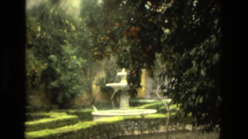 A 1978 8mm travel frame in Seville shows a small stone fountain set within clipped hedges and dense garden foliage.
