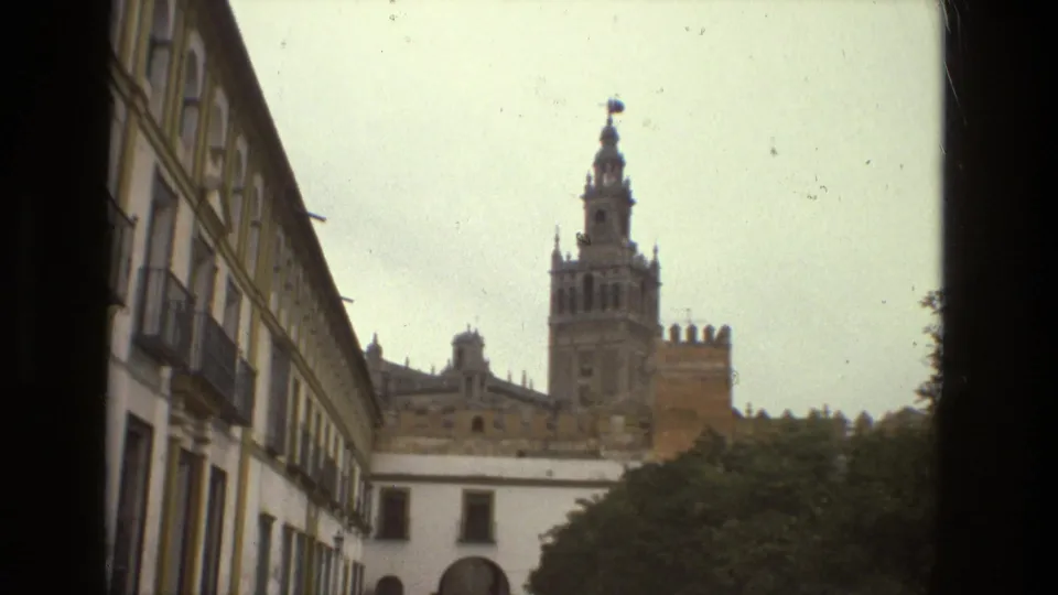 A street-level Seville view shows a long building with balconies and arched windows leading the eye toward the cathedral and Giralda tower.