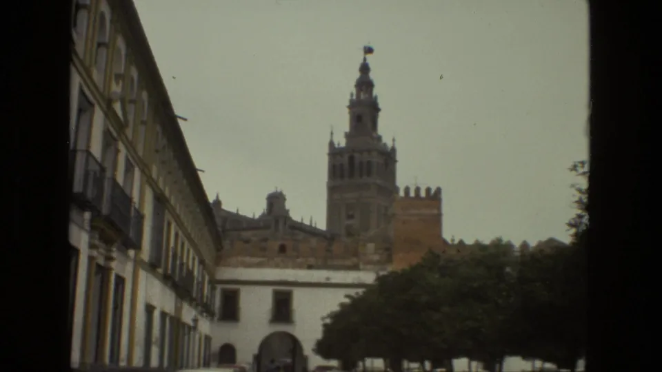 A later frame repeats the Seville cathedral view, with the Giralda tower rising beyond a long balconied facade and shaded street trees.