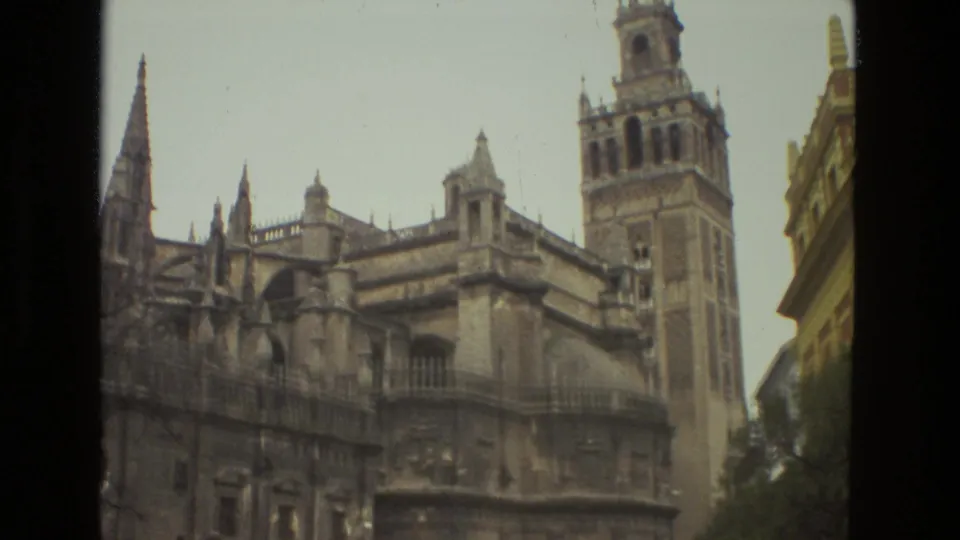 Vintage 8mm frame of Seville Cathedral, with ornate roofline details and the Giralda tower beside a neighboring building edge.