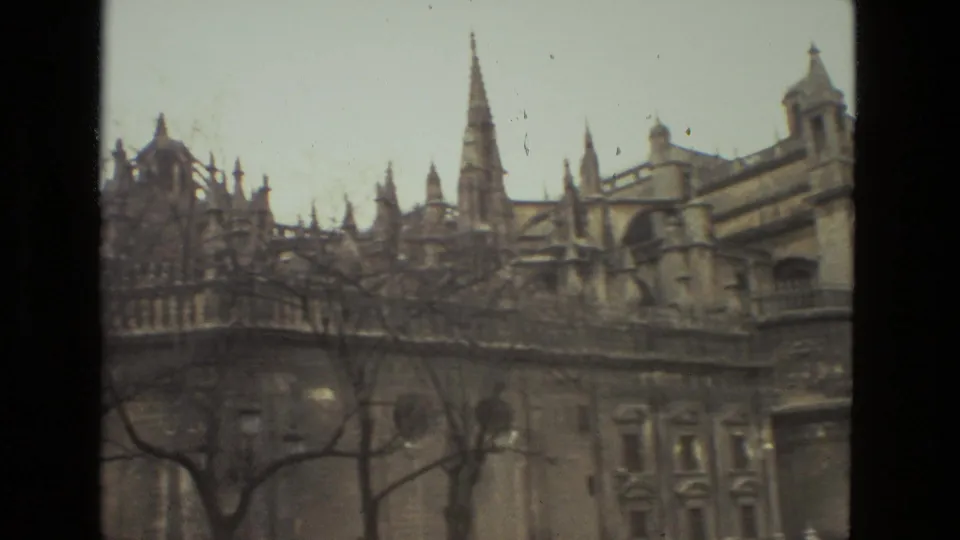 1978 Seville Cathedral exterior seen from below, with Gothic spires, stone facade, and leafless branches across the frame.