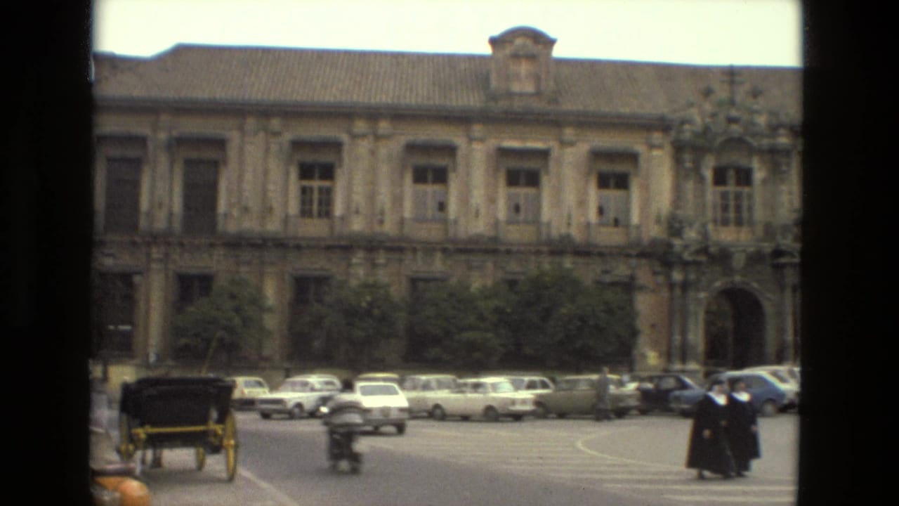 Nuns in dark habits cross a Seville street in 1978, with vintage cars and an ornate historic facade behind them.