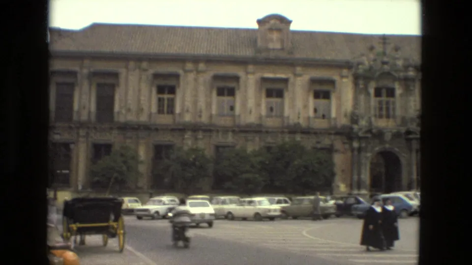 Nuns in dark habits cross a Seville street in 1978, with vintage cars and an ornate historic facade behind them.