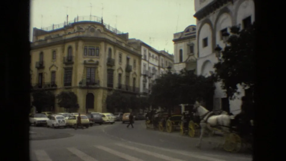 1978 Seville street corner with ornate buildings, parked cars, pedestrians, and horse-drawn carriages moving through the intersection.