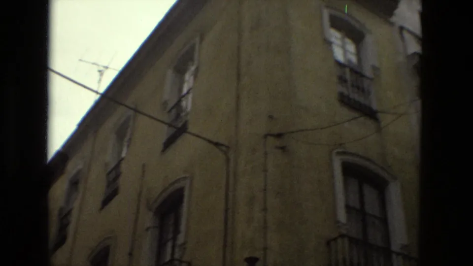 1978 Seville frame showing upper floors of a weathered stucco building with small balconies, dark windows, and utility wires overhead.
