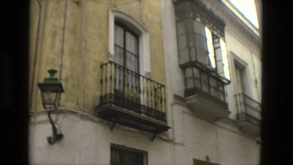 1978 Seville home-movie frame with pale and yellow stucco facades, wrought-iron balconies, shuttered windows, and a mounted street lamp.