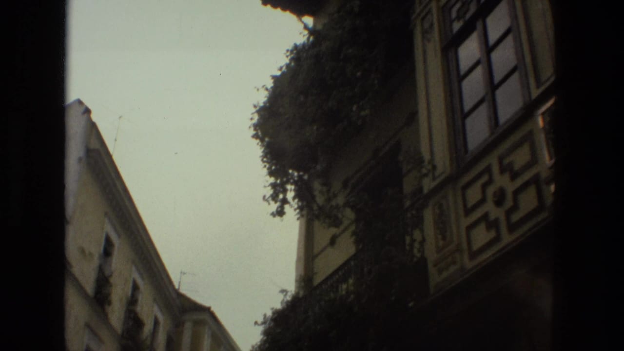 1978 8mm view down a narrow Seville street, showing balconies, pale facades, greenery, and strong handheld framing.