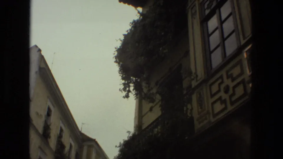 1978 8mm view down a narrow Seville street, showing balconies, pale facades, greenery, and strong handheld framing.
