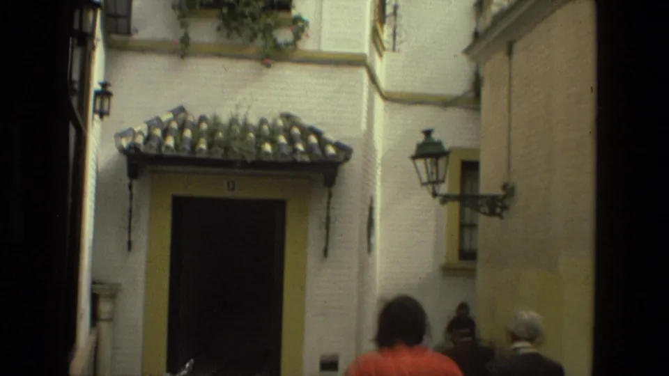 1978 Seville street detail showing a tiled doorway, whitewashed wall, yellow trim, wall lantern, and pedestrians at the lower edge.