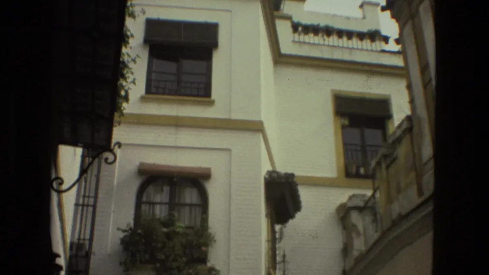 1978 Seville home-movie frame of upper whitewashed walls, window guards, balcony railings, plants, and shaded alley framing.