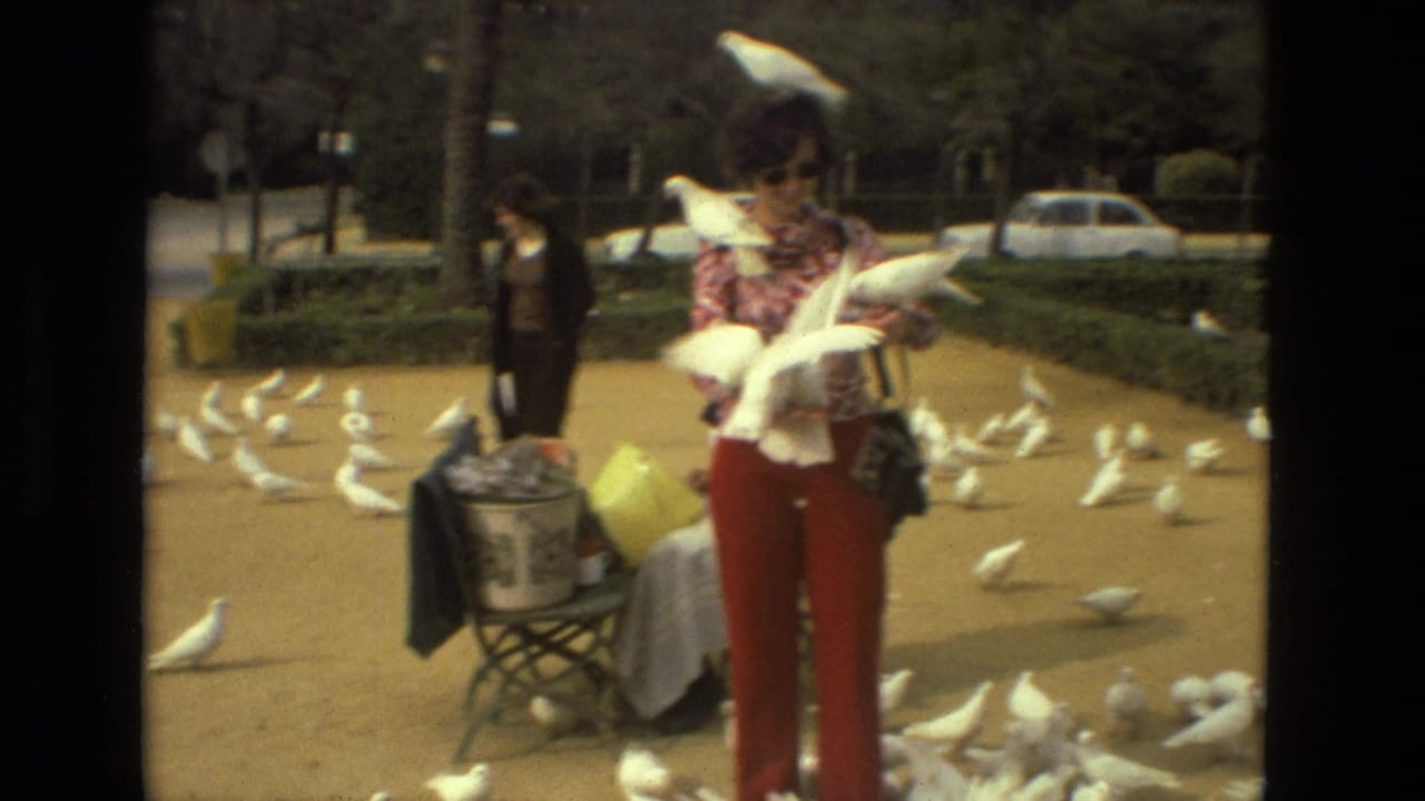 A woman in red pants and a patterned top holds white pigeons in a Madrid square, with more birds spread across the ground.