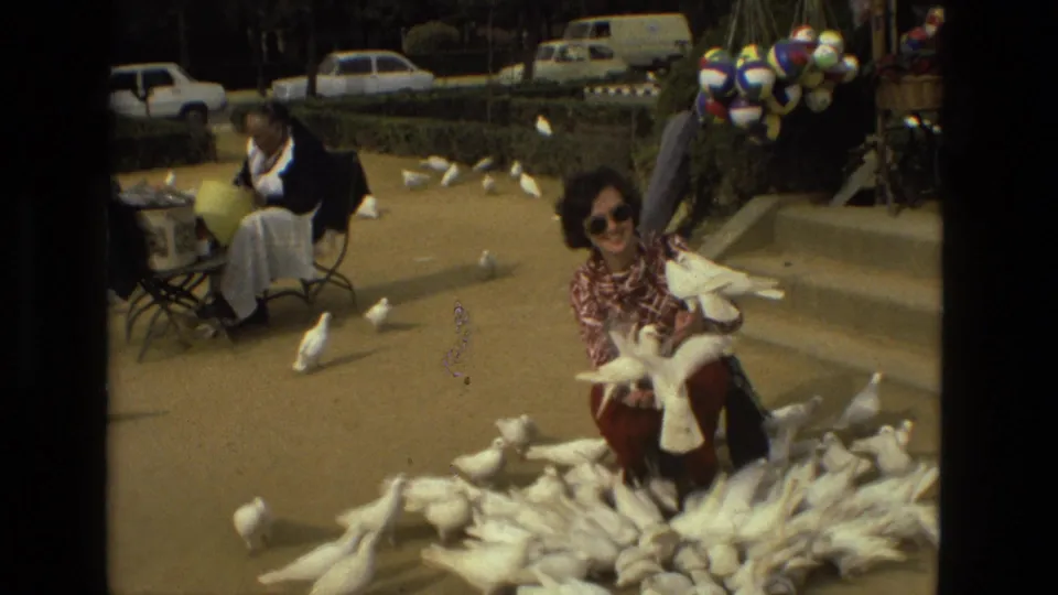 1978 Madrid frame of a smiling crouching woman surrounded by white doves, with a seated feeder and colorful balloons behind her.
