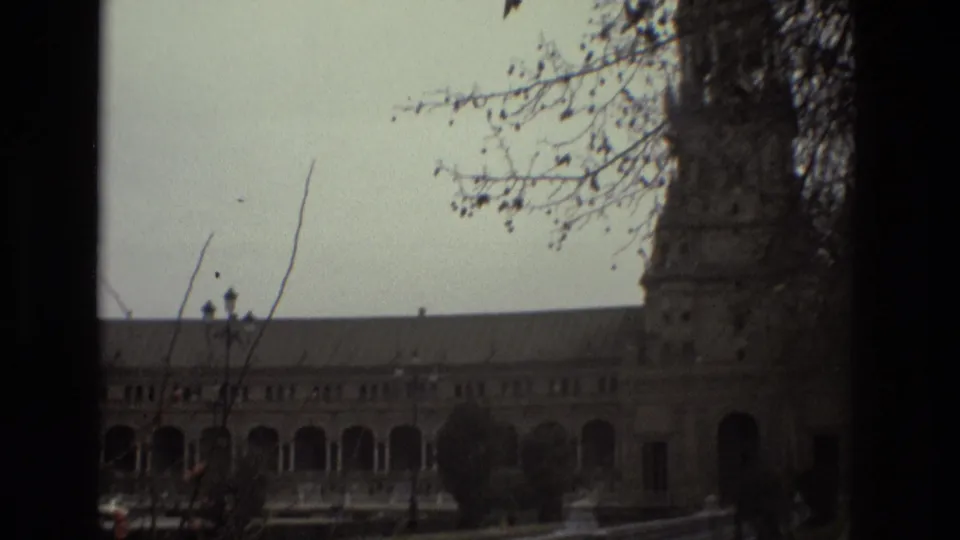 1978 Madrid 8mm frame of an ornate palace facade with arched colonnades, a tower, and bare tree branches in the foreground.