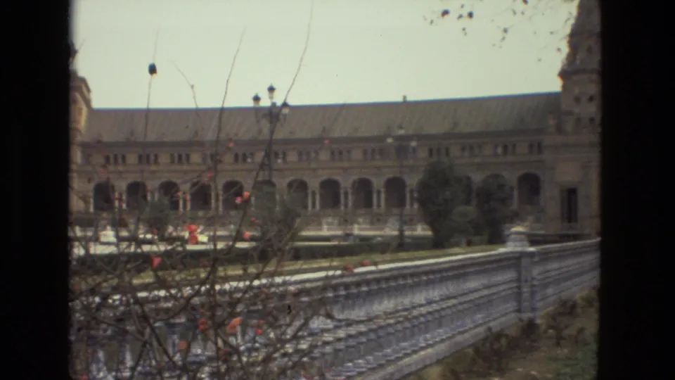 1978 Madrid 8mm frame showing the palace's arched facade beyond a stone railing and foreground branches.