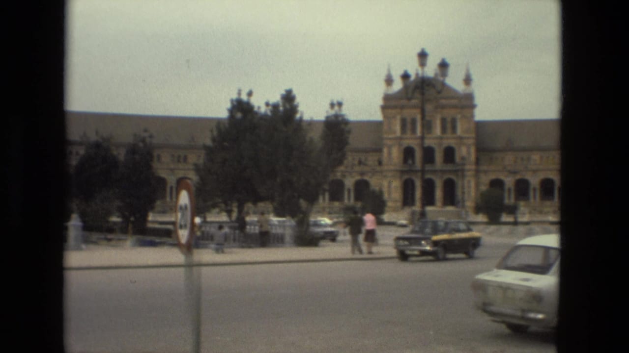 Historic building across a street with cars, pedestrians, trees, and a roundabout sign.
