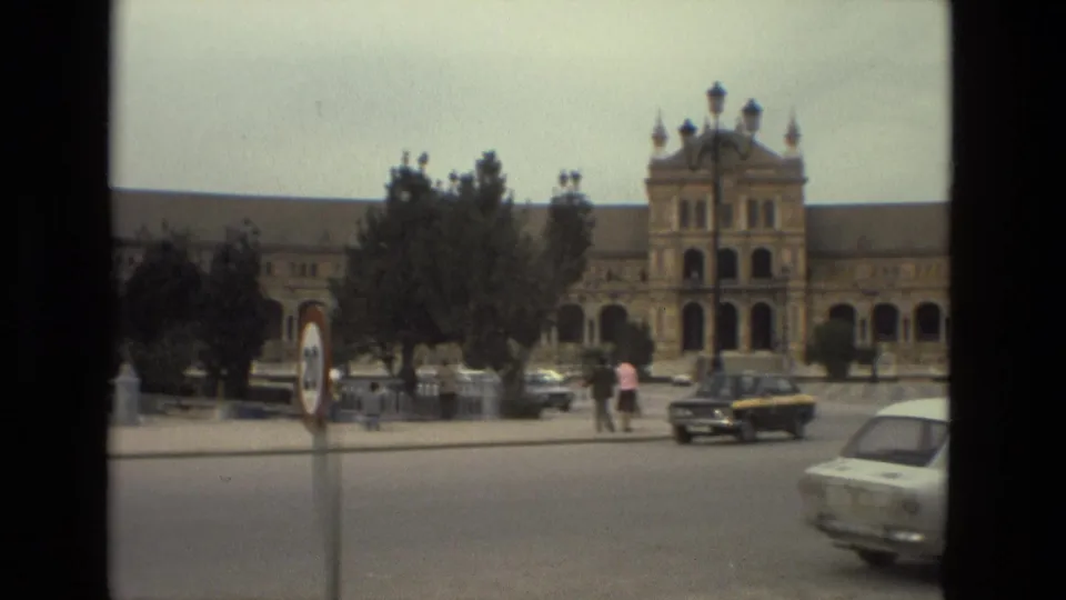 1978 Madrid street view with older cars, pedestrians, a roundabout sign, and a large historic building in the background.