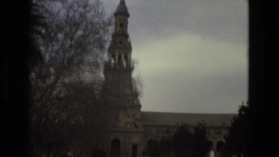 Soft 1978 Madrid 8mm view of a towered historic building and bare trees, with the street edge and sign partly visible.