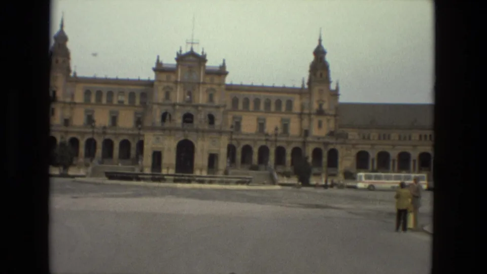 The camera holds on the monumental facade, with a bus and small distant pedestrians visible along the right side of the plaza.