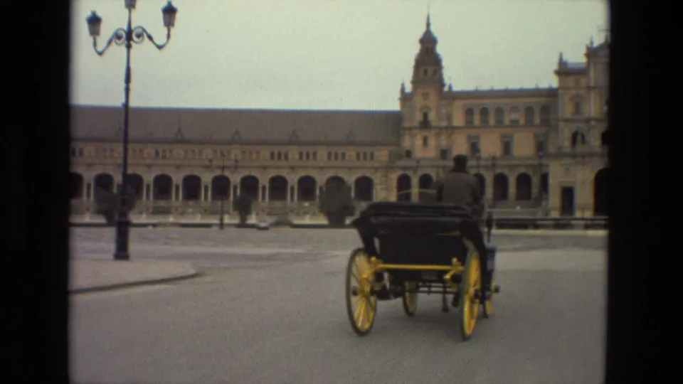The carriage continues across Madrid's Plaza de España, framed by a broad paved square and ornate building facade.