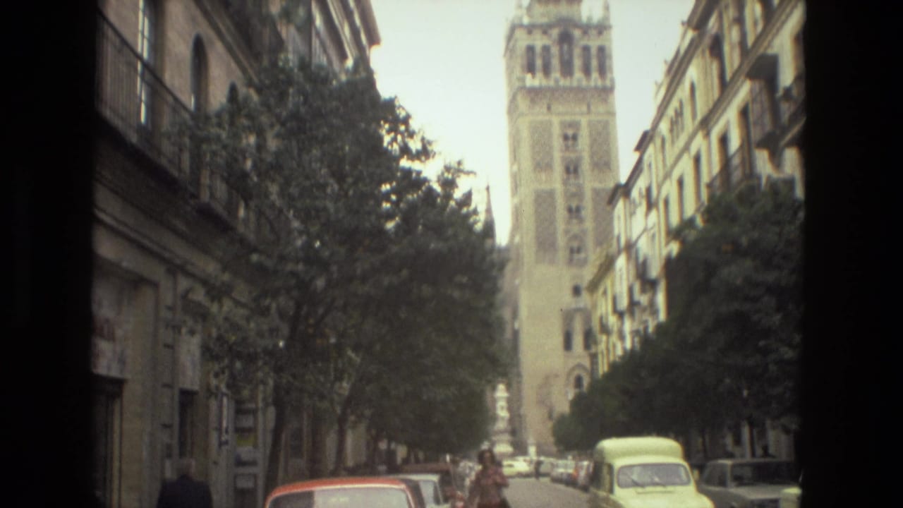 Tall ornate tower above a tree-lined street with parked cars and apartment facades.