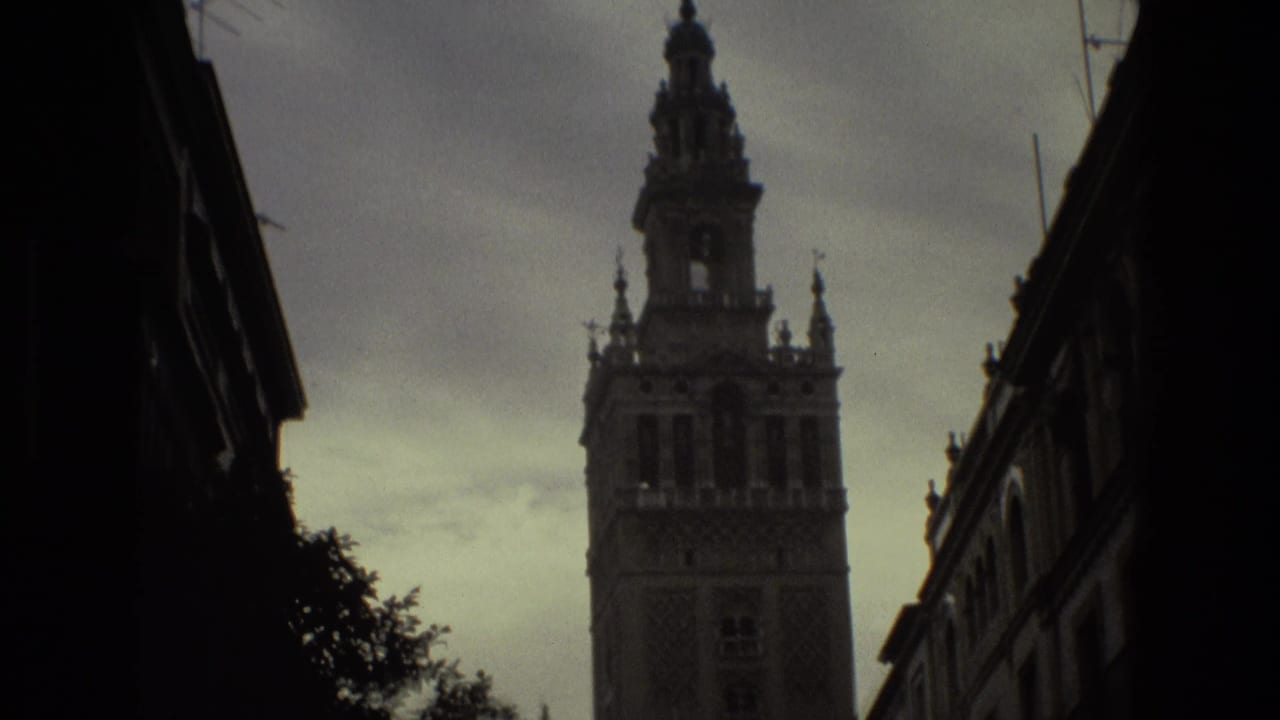 Dark low-angle street view with a tall historic tower rising against a cloudy sky.