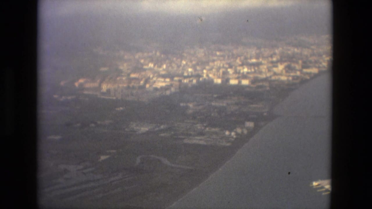 Aerial city view through an aircraft window with wing edge and hazy skyline.