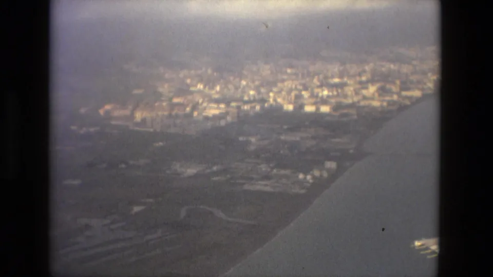 1978 Barcelona aerial approach view showing a hazy urban area, low hills, and the aircraft wing at the window edge.
