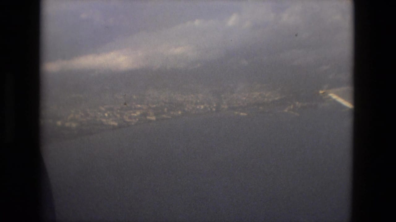 Airplane-window view over water toward a hazy coastal city.