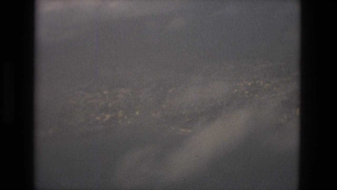 Cloudy sky above a distant city, seen through dark film-frame borders.