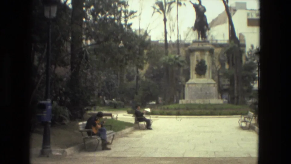 1978 Barcelona park scene with seated people, benches, palm trees, greenery, and an equestrian statue in a public square.