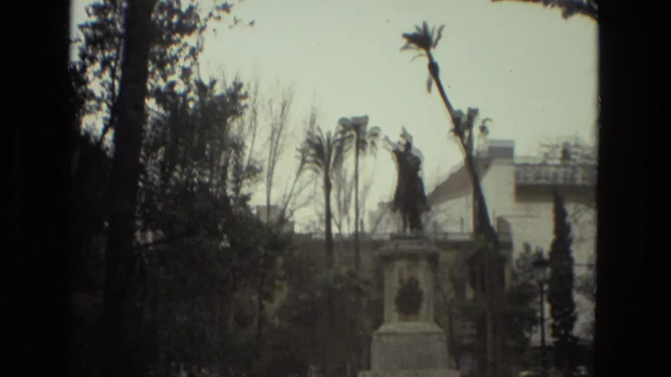 1978 Barcelona 8mm frame with an equestrian statue rising above trees and palms, partly obscured by dark frame edges.