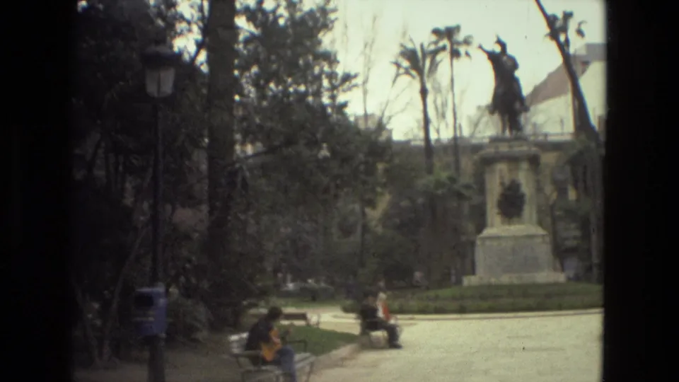 1978 Barcelona park frame showing the equestrian monument, surrounding paths, a lamppost, benches, and seated visitors in a sunny public space.