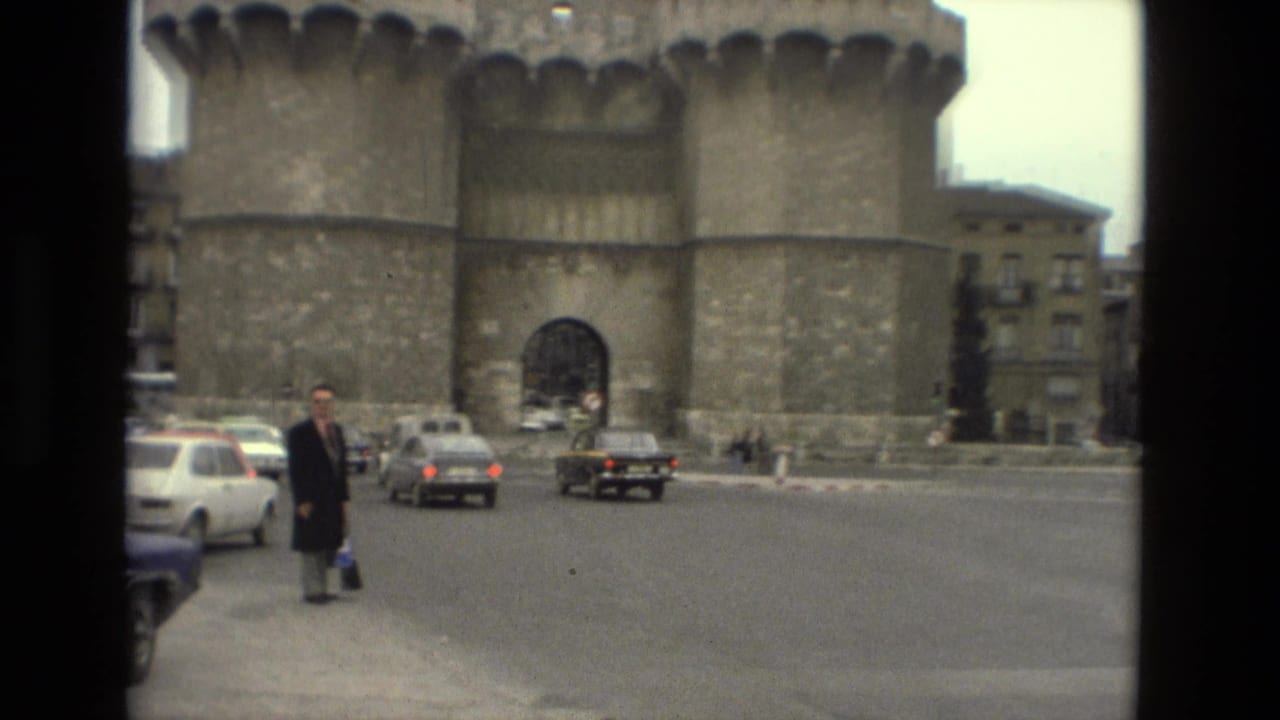 Wide street view with a suited man near cars in front of a large stone monument.