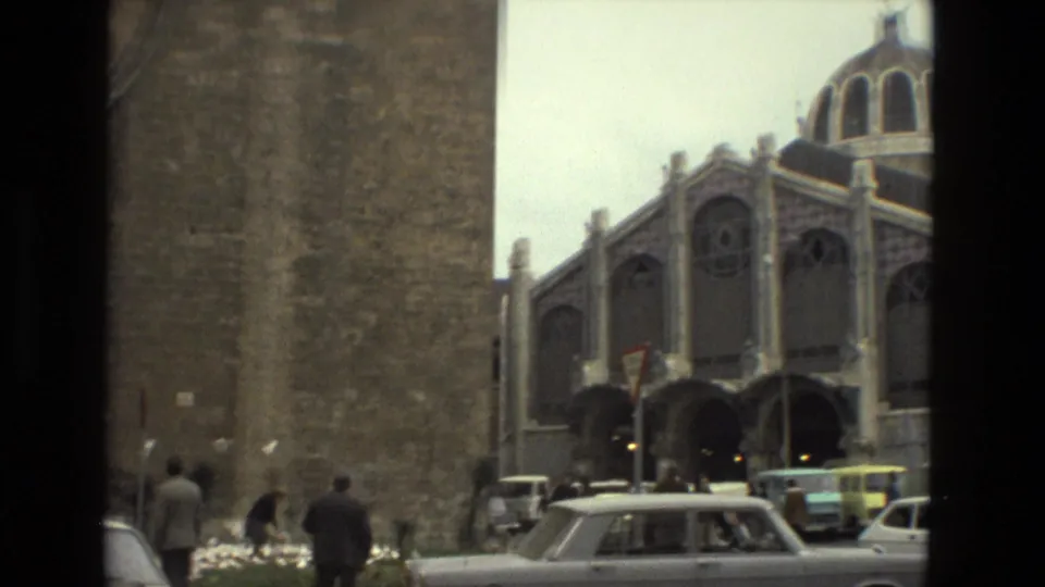 1978 Barcelona home-movie frame of a large domed building with arched windows, seen across a street with cars in the foreground.