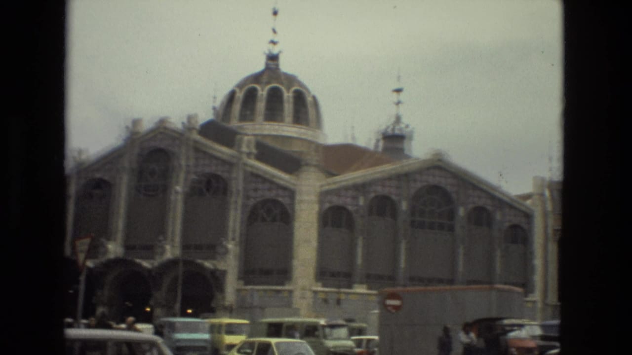 Domed building with arched windows beside street traffic and parked cars.