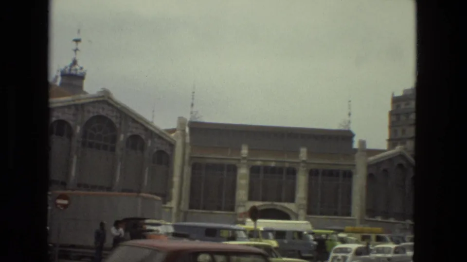 Barcelona street view with an arched public building facade, period buses, cars, and pedestrians visible in 1978 home-movie footage.